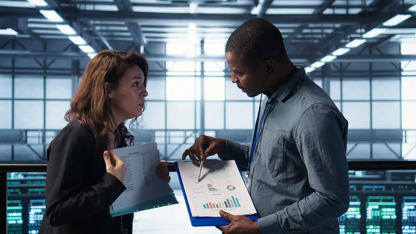 Команда центра обработки данных изучает бумажные документы в серверной, проверяя систему.